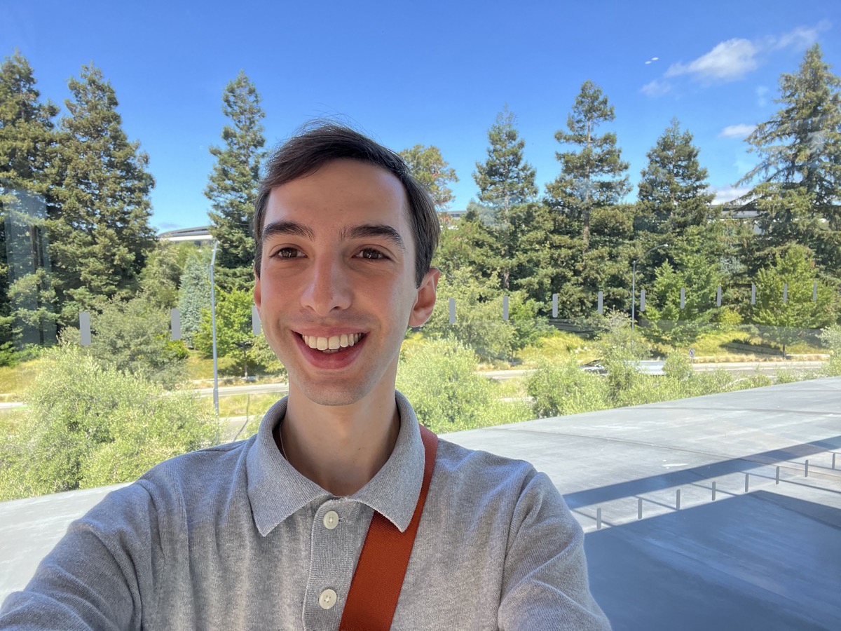 Lorenzo Confalonieri, smiling outdoors in front of trees and a walkway, wearing a grey polo shirt.